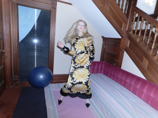Abby Champion in a patterned black and gold dress standing in an interior hall with a wooden staircase and pink daybed.