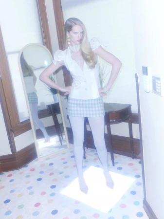 Model Abby Champion standing on a lit floor wearing a white sleeveless top and checkered skirt for Rouge Fashionbook