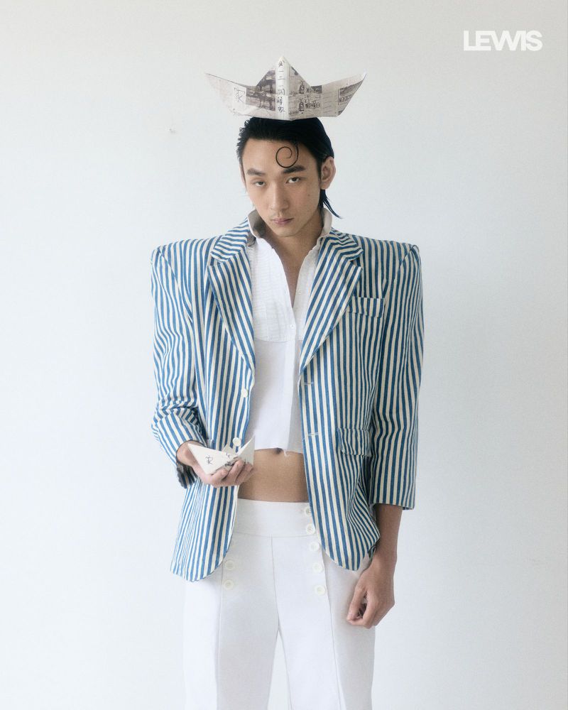 Man wearing a blue-and-white striped blazer, white shirt, and paper boat hat for Lewis Magazine project LIFE’s A JOURNEY