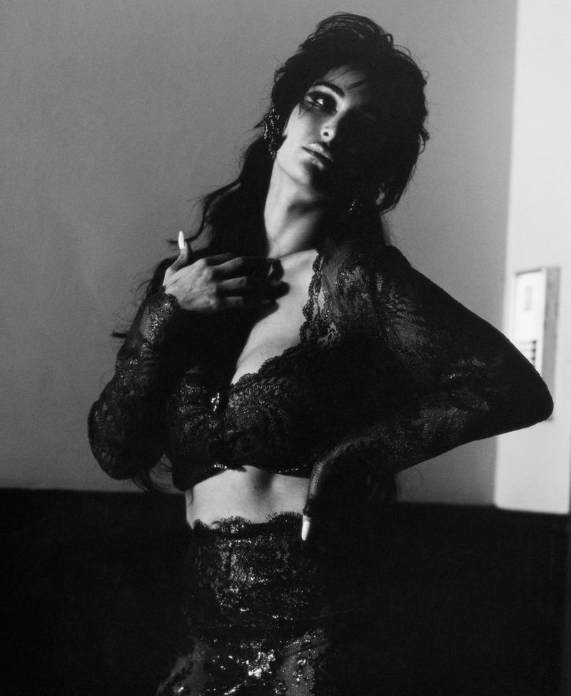 Black and white portrait of a woman in black lace lingerie posing against a plain background for i-D Magazine.