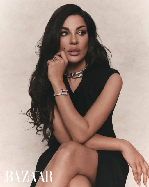 Nadine Njeim in a black dress wearing serpent jewelry against a textured backdrop for Harper's Bazaar Arabia
