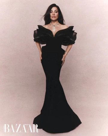 Nadine Njeim wearing a black ruffled evening gown and diamond necklace against a textured pink-beige backdrop
