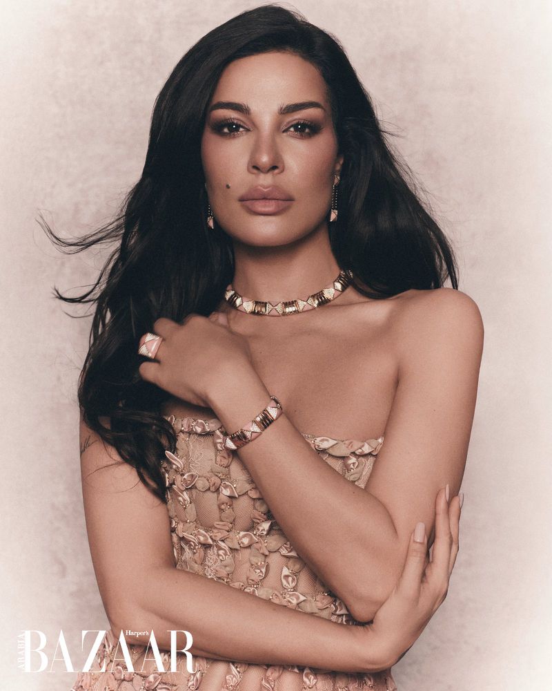 Portrait of Nadine Njeim wearing an embellished strapless dress and statement jewelry against a textured backdrop for Harper's Bazaar Arabia.