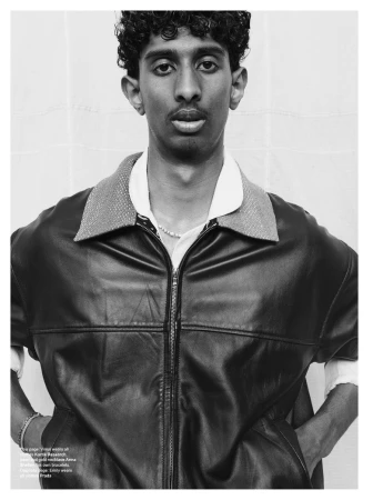 Portrait of young man with curly hair wearing dark leather jacket over white collared shirt against a white seamless backdrop