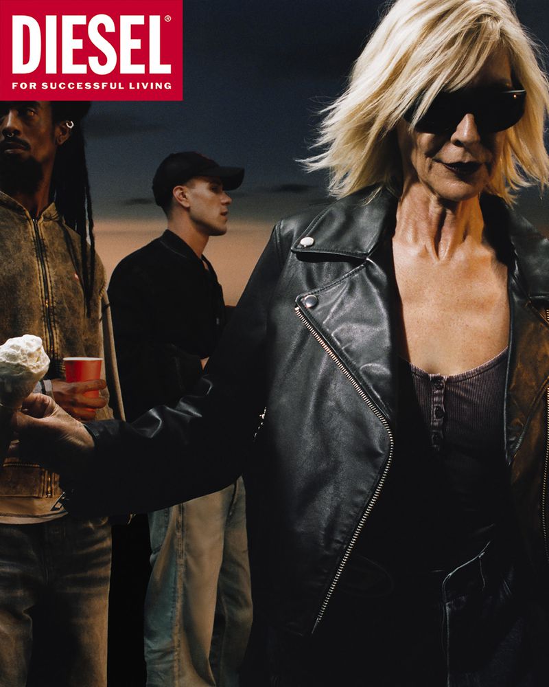 An older blonde woman in a black leather jacket and sunglasses holding an ice cream cone, with two men standing in the background.