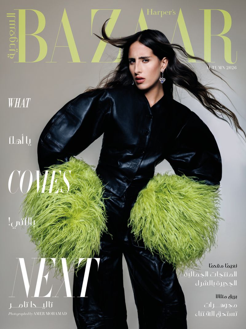 Model Taleedah Tamer wearing a black leather outfit with vibrant green feathered cuffs against a plain grey backdrop.