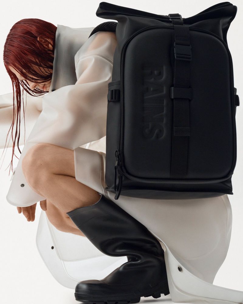Black Rains backpack is the primary focus, complemented by a person in a white translucent coat and black boots, set against a clean background.