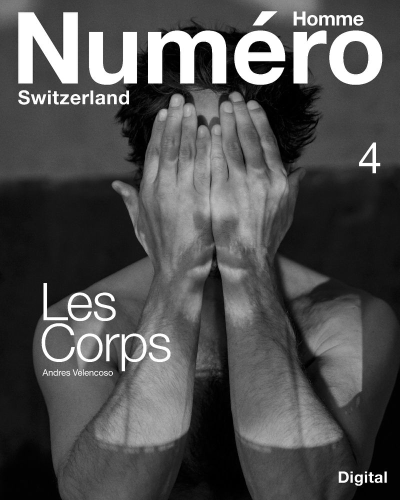 Monochrome portrait of Andres Velencoso holding his hands up to cover his face against a dark background