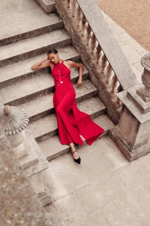 Model lying on grand outdoor stone staircase wearing a long red halter neck dress and black shoes