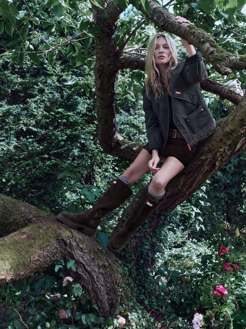 Model Kate Moss sitting in a large tree wearing green rubber boots and an olive jacket for Hunter Boots