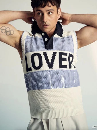 Portrait of a young adult male wearing a sleeveless collared shirt with the word 'LOVER' against a neutral background.