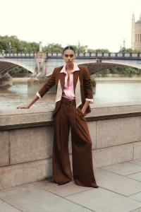 Model in brown trousers and matching blazer with pink shirt posing against stone bridge and river for ME+EM