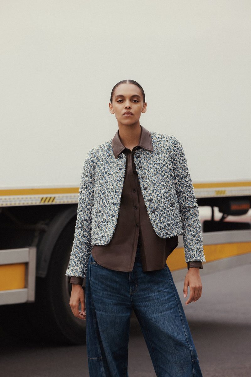 Model wearing tweed jacket and blue denim jeans standing in front of a white delivery truck.