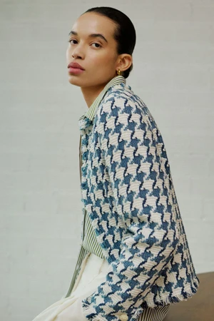 Model wearing a blue and white houndstooth jacket and striped shirt against a white brick wall