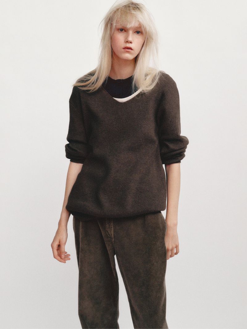 Model with long blonde hair wearing a dark brown V-neck sweater against a plain white studio background.