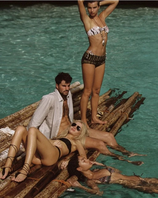 Four people wearing swimwear on a raft in turquoise water, modeling fashion in an outdoor beach setting with bright natural light.