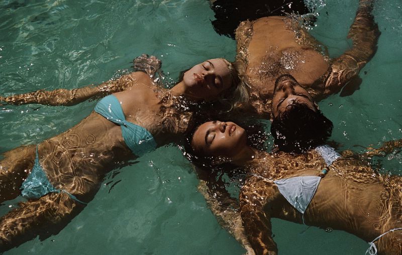 Three people, two women and one man, are floating in clear, turquoise water, wearing bathing suits on a sunny day.