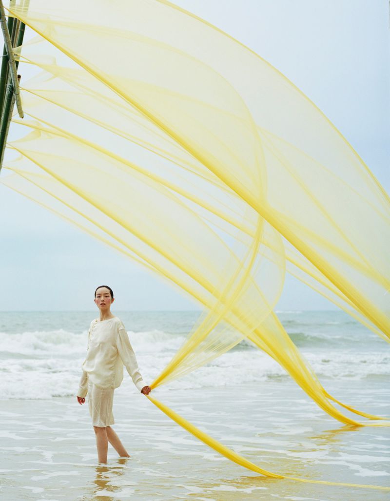 Model FeiFei Sun holding yellow fabric on a beach with ocean waves for Vogue China