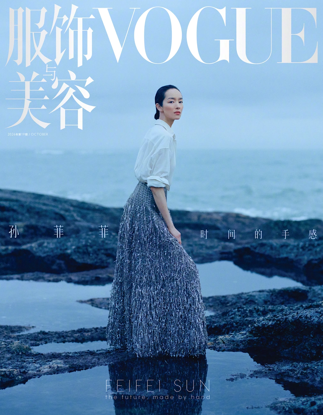Model FeiFei Sun wearing a white shirt and textured skirt standing on a rocky coast by the ocean for Vogue China.