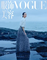 Model FeiFei Sun wearing a white shirt and textured skirt standing on a rocky coast by the ocean for Vogue China.