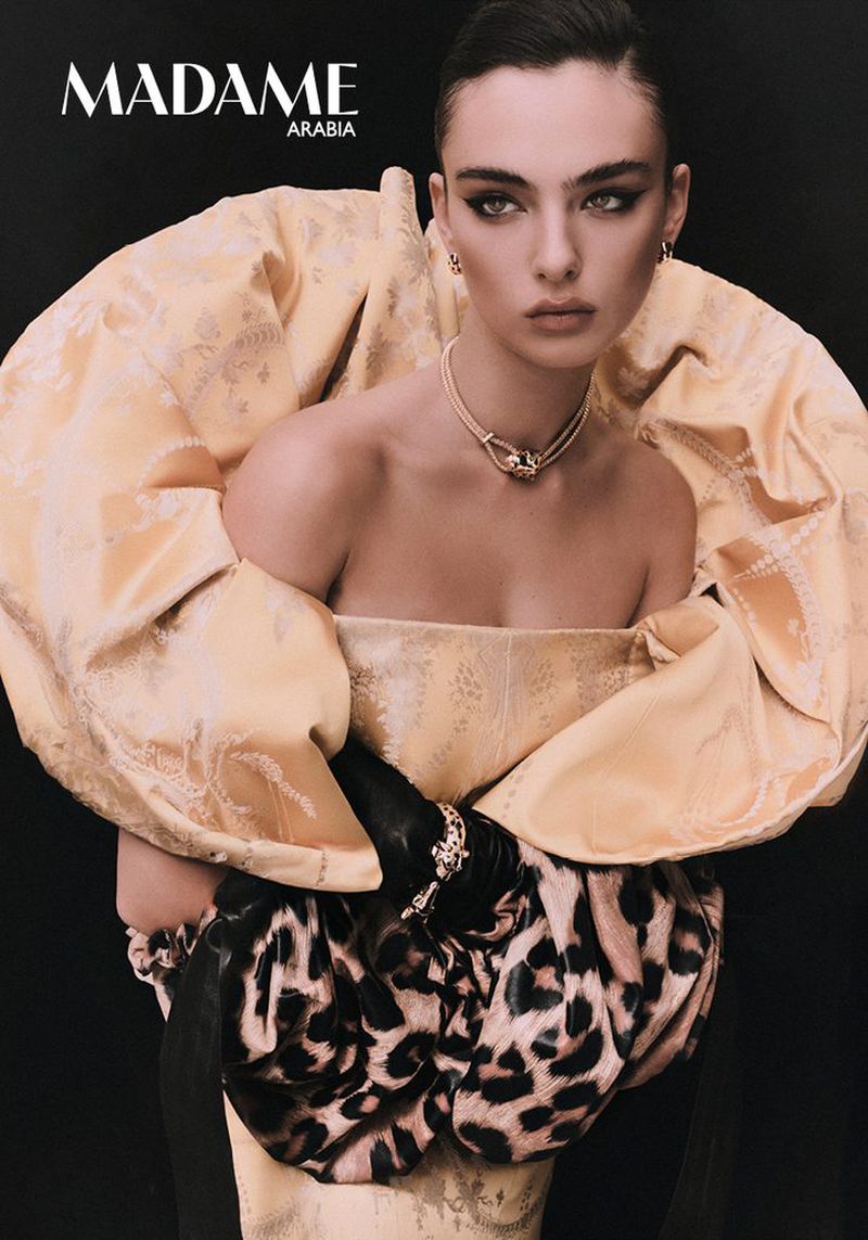 Model Deva Cassel wearing an ornate yellow sculptural top and dark gloves against a black background