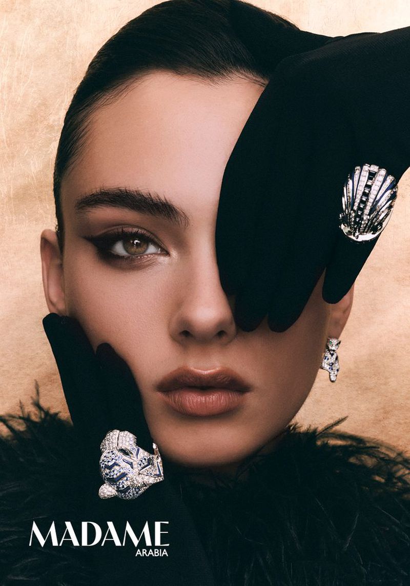 Deva Cassel wearing black gloves and jewelled rings with winged eyeliner against a textured golden background