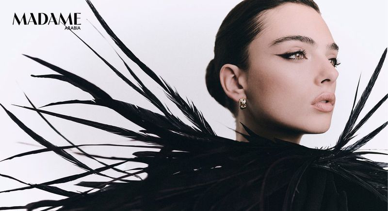 Close-up portrait of model Deva Cassel wearing a black feathered collar against a white background.