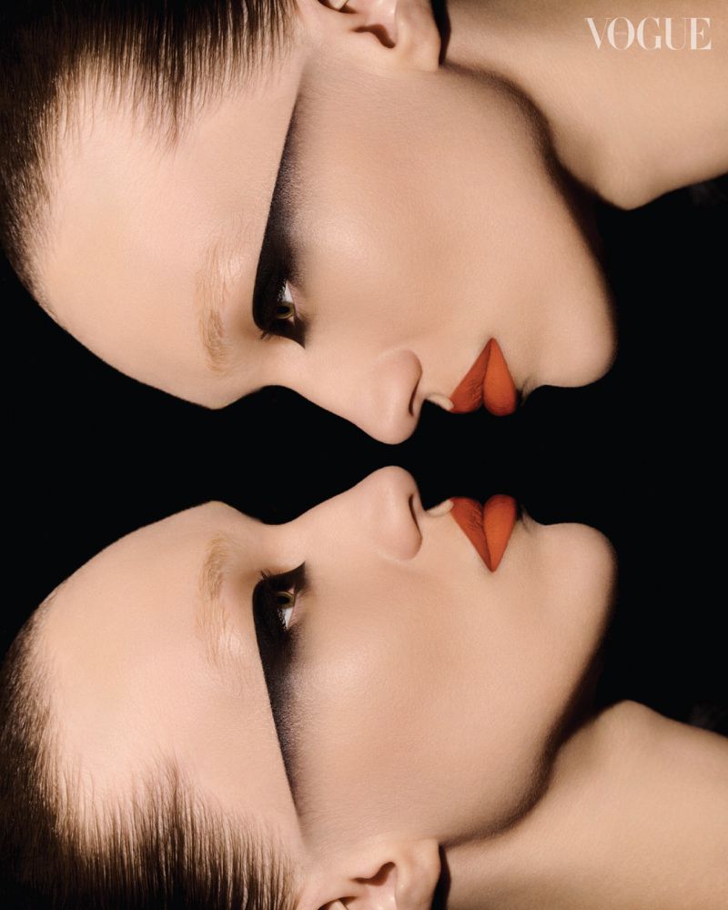 Close-up profile portraits of two female models in dramatic dark eye makeup and vivid red lipstick mirrored vertically.