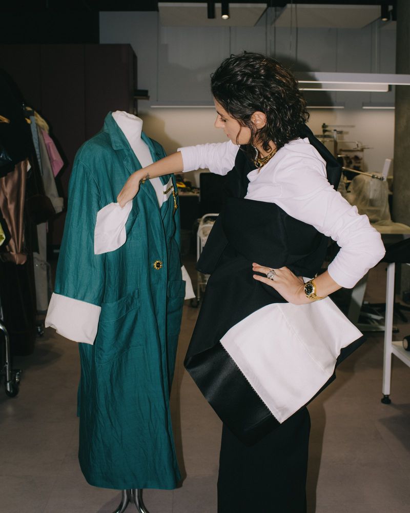 A woman adjusting a teal coat on a mannequin in a studio workspace for an i-D Magazine feature