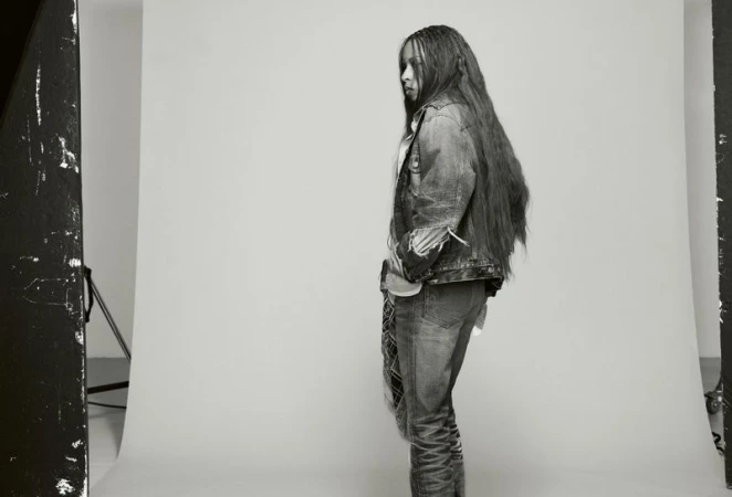 Black woman wearing a denim jacket standing against a grey seamless studio backdrop in profile view