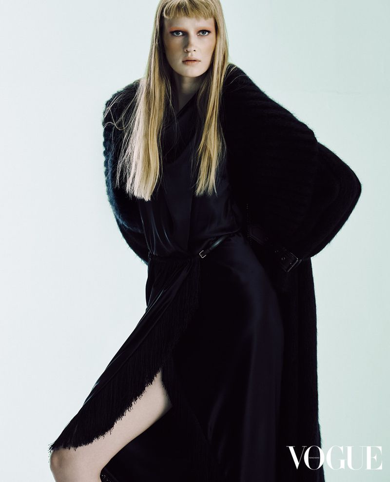 Model with long blonde hair in a dark coat and dress against a white background for Vogue Hong Kong