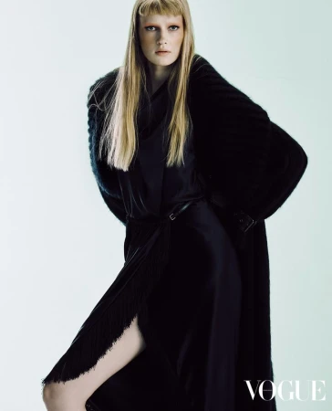 Model with long blonde hair in a dark coat and dress against a white background for Vogue Hong Kong