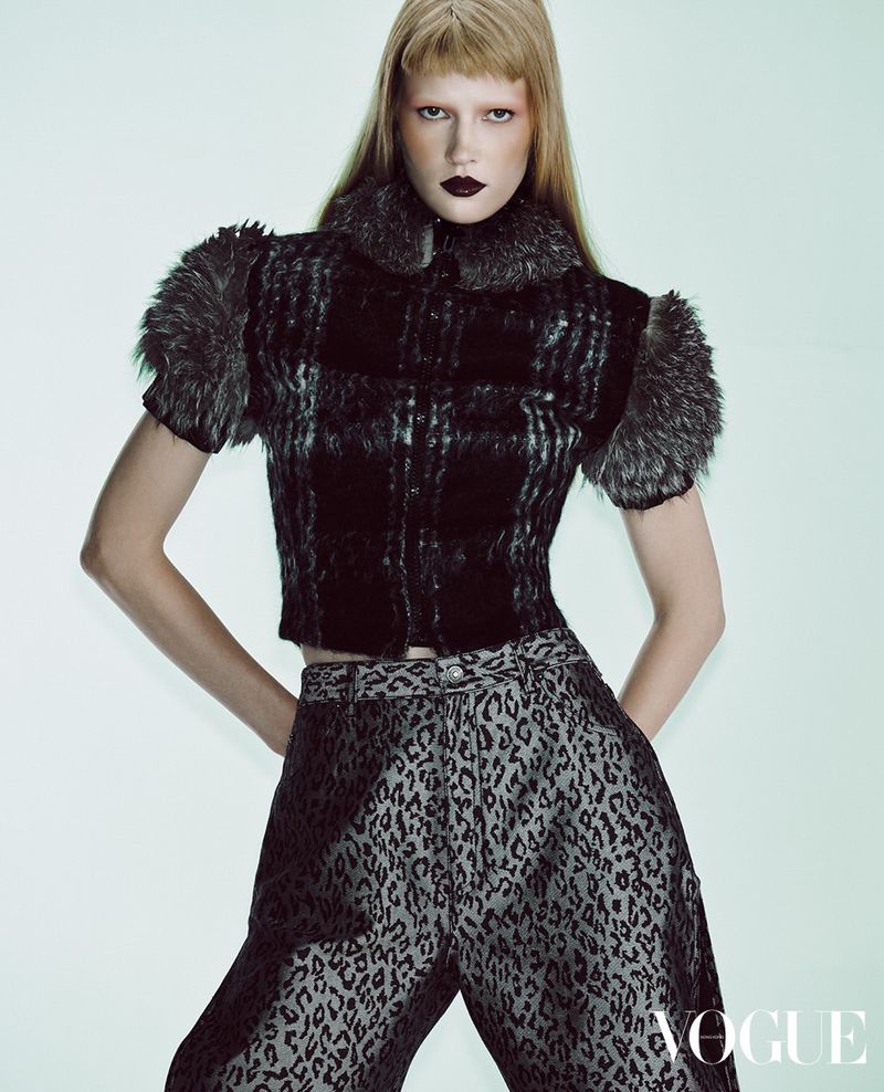 Model with dark lips and blonde hair wearing a textured dark top and animal print trousers against a light backdrop