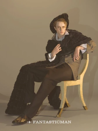 Model seated on a decorative chair wearing a dark beret, cape, and trousers for Fantastic Man China.
