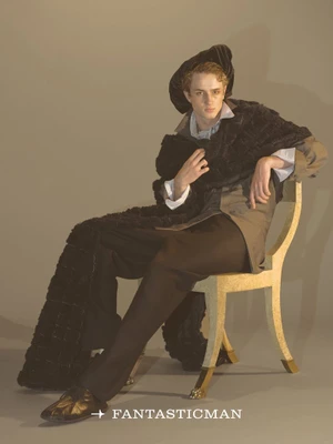 Model seated on a decorative chair wearing a dark beret, cape, and trousers for Fantastic Man China.