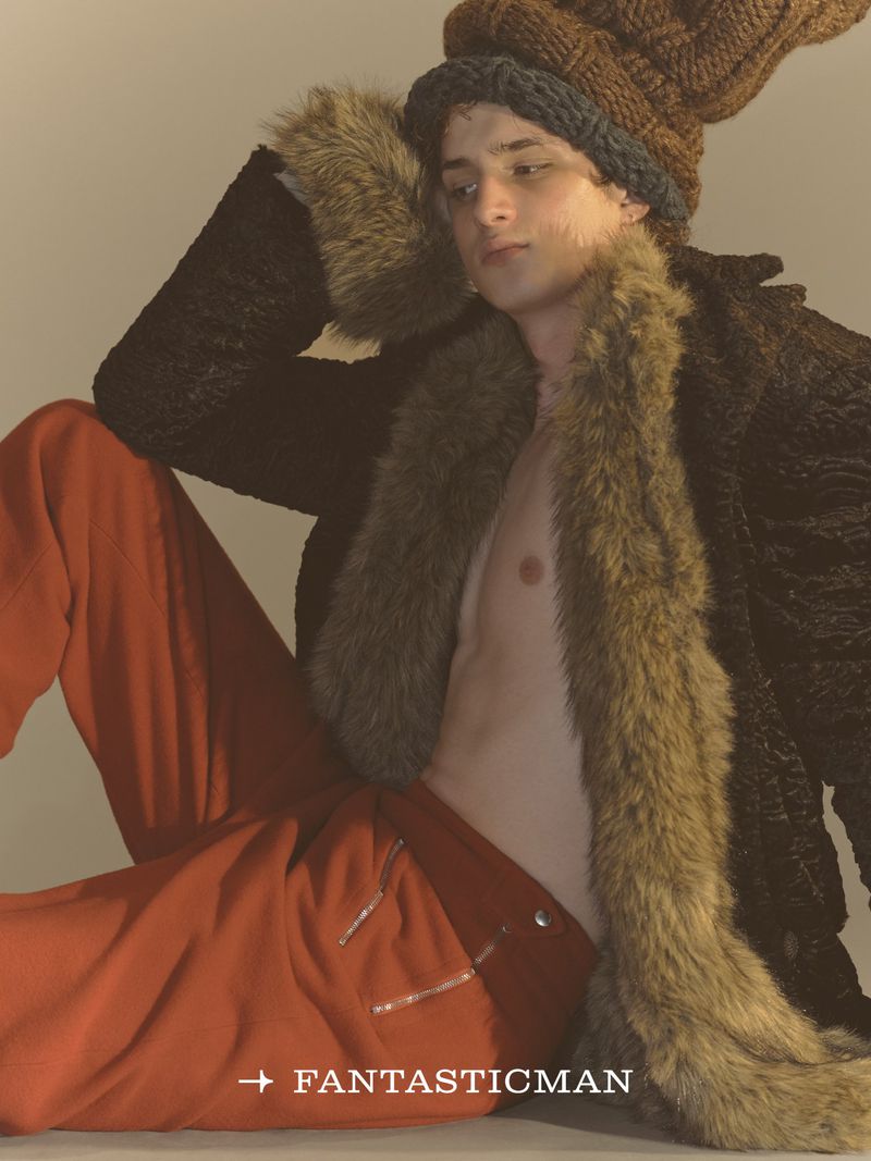 Model wearing a large knit hat and fur-trimmed coat with orange trousers for Fantastic Man China.