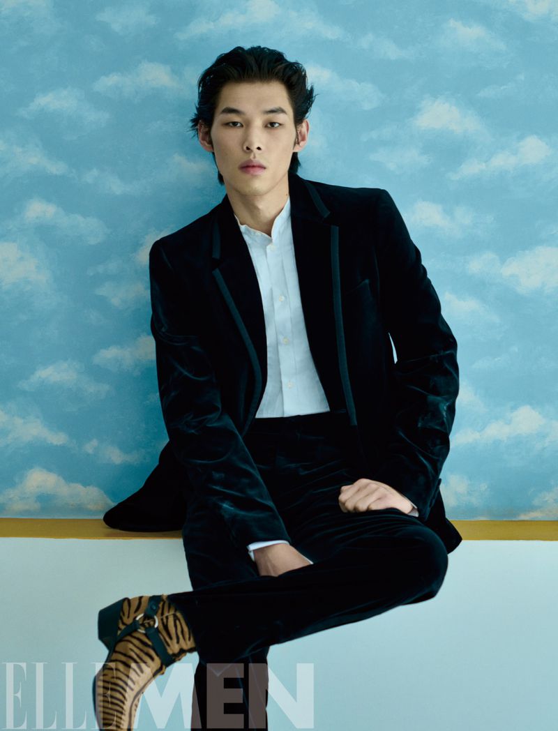 Young man in a black velvet suit and patterned boots seated against a painted cloud backdrop for Elle Men China.