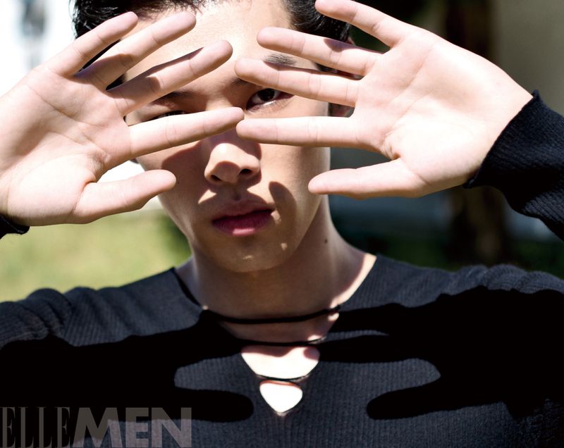 Close-up portrait of a male model holding his hands up to his face, casting shadows across his features.