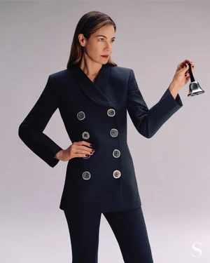 Michelle Monaghan in dark double-breasted jacket holding a small bell against a neutral backdrop for S Magazine