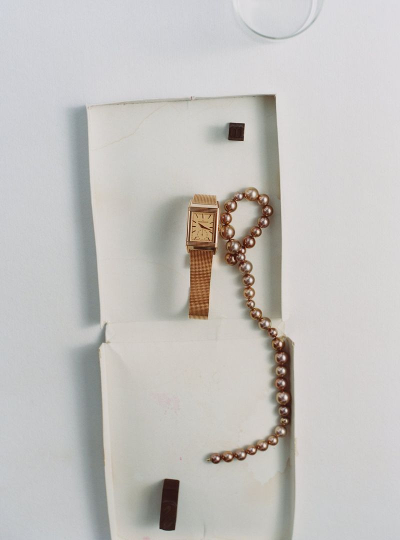 Overhead flat lay of a gold watch and beaded necklace inside an open white paper box
