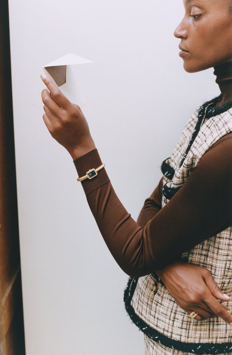 Woman in tweed vest holding a folded paper airplane against a plain white background for Monocle Magazine.