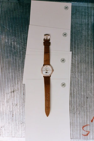 Brown leather strap watch with a white dial placed on a stack of white paper stationery over corrugated metal