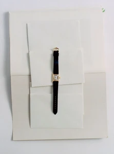 Gold wristwatch with black leather strap placed vertically across layered white envelopes and paper sheets.