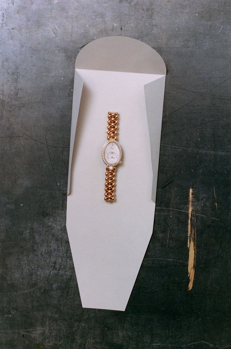 Gold luxury wristwatch placed inside a custom white folded paper sleeve on a dark textured surface.