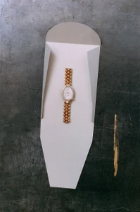 Gold luxury wristwatch placed inside a custom white folded paper sleeve on a dark textured surface.