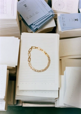 Gold chain necklace resting atop a stack of lined white and light blue paper stationery.