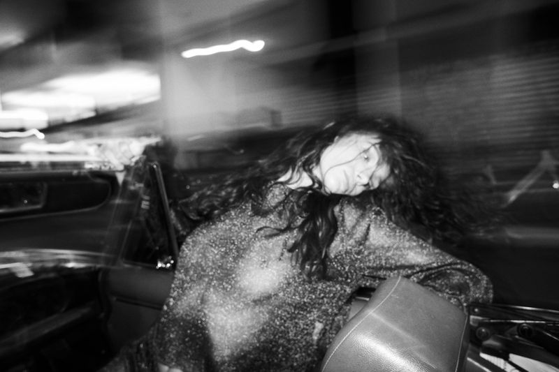 Monochrome action shot of a person with long dark hair leaning inside a car with motion blur and light trails.