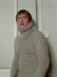 Man wearing a fluffy grey turtleneck sweater standing against a textured wall with switches
