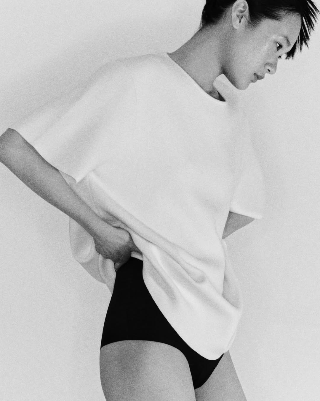 Woman wearing a white t-shirt and black bottoms poses against a neutral backdrop in a black and white studio fashion shot.