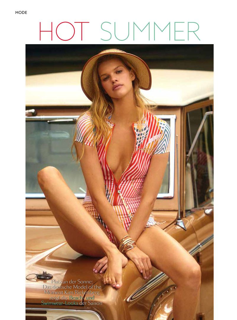 Fashion editorial photo features an adult female model with long hair in a multicolored swimsuit and straw hat, sitting on a car.